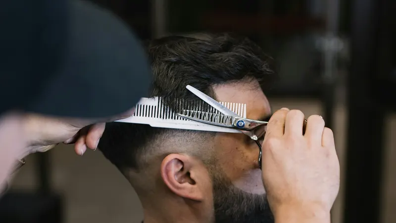 A stylist cutting a client's hair with scissors over comb in a salon.