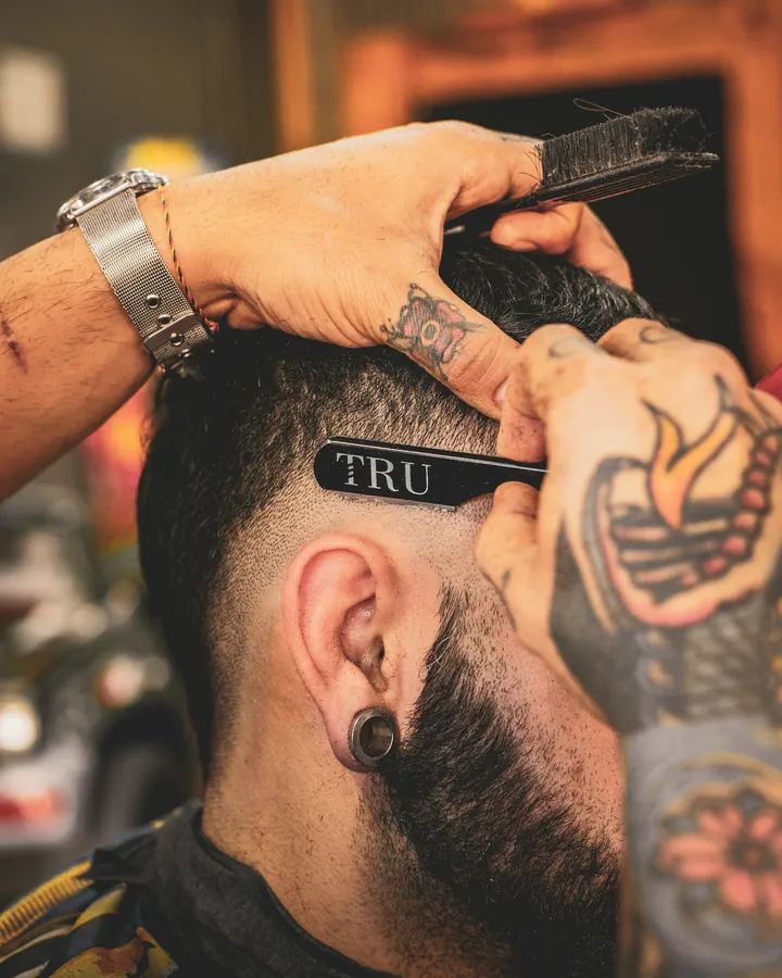 A barber using a straight razor to line up a client's fade in a barbershop chair.
